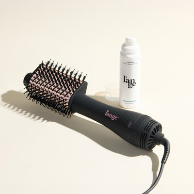 The Effortless Blowout Duo Value Set, featuring a Black Le Volume Eleve brush and Glass Hair spray, displayed against a beige background